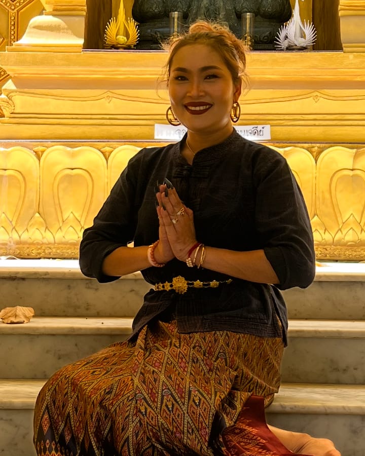 Portrait of Bee in traditional Thai dress, smiling with her hands pressed together